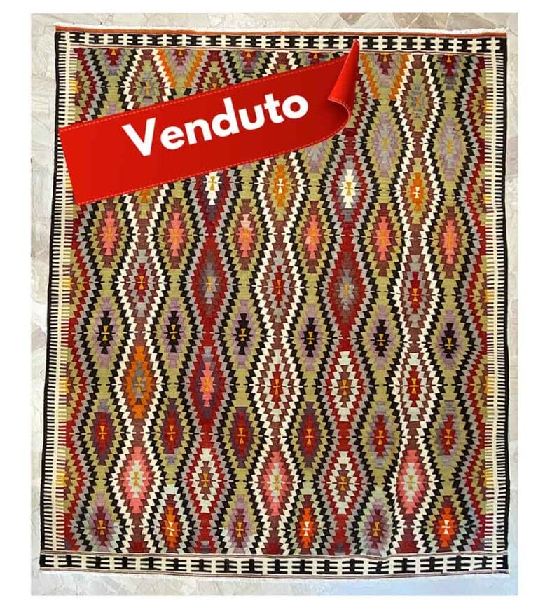 Un kilim colorato con motivo geometrico e un nastro rosso con la scritta 