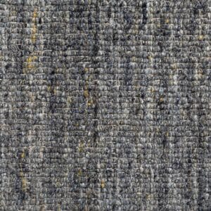 Primo piano di un tappeto grigio con sottili macchie gialle e blu. La superficie, che ricorda il disegno di una bozza automatica, presenta fibre intrecciate in modo fitto, creando un aspetto morbido e denso.