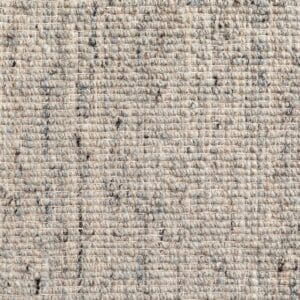 Primo piano di un tessuto beige e grigio dall'aspetto grossolano e strutturato, che ricorda un tappeto artigianale. Le fibre visibili e le sottili variazioni di colore gli conferiscono un aspetto naturale e leggermente rustico.