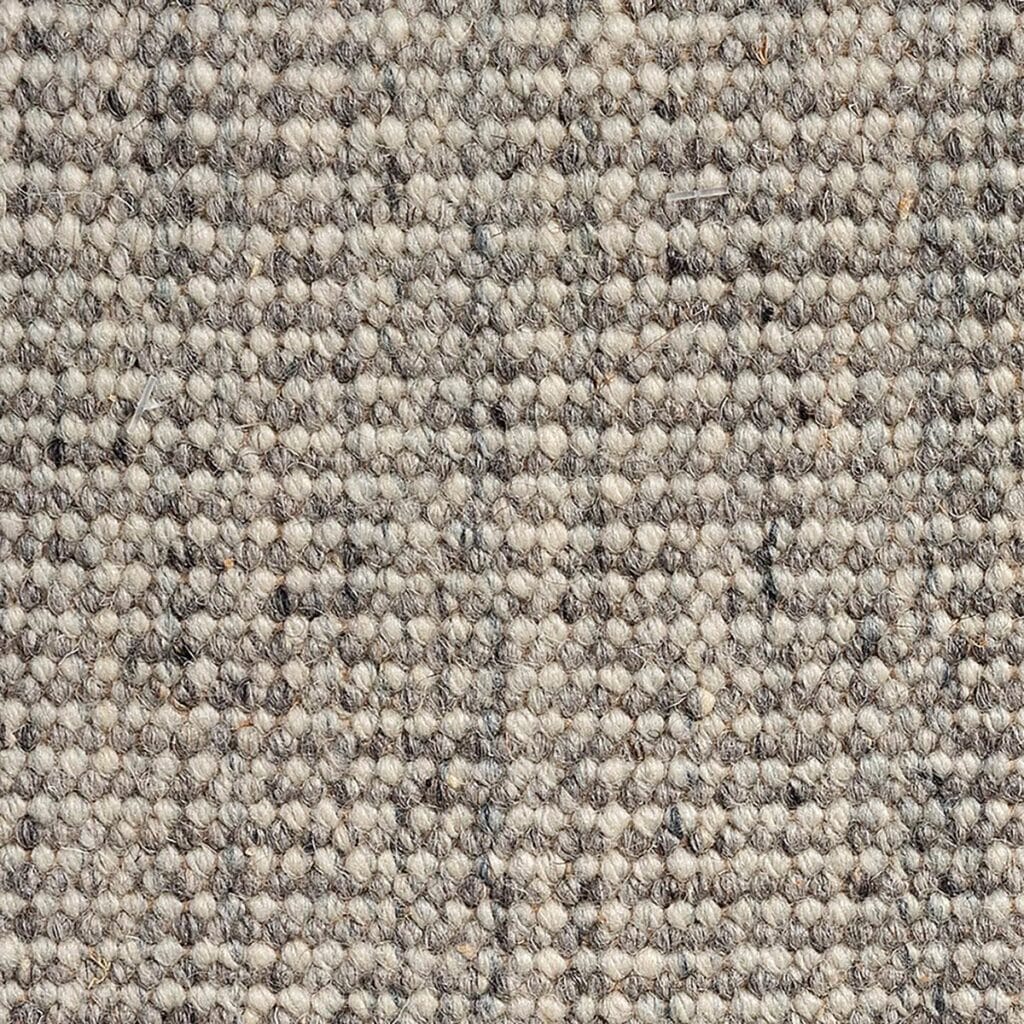 Vista ravvicinata di un tappeto beige testurizzato, con un sottile motivo di tessitura. Le fibre creano un aspetto a griglia, che ricorda gli stili di bozza automatica, mostrando diverse tonalità di beige e marrone chiaro.