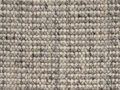 Vista ravvicinata di un tappeto beige testurizzato, con un sottile motivo di tessitura. Le fibre creano un aspetto a griglia, che ricorda gli stili di bozza automatica, mostrando diverse tonalità di beige e marrone chiaro.