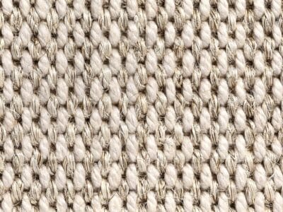 Primo piano di un tessuto strutturato che ricorda il sisal boucle, con spesse fibre beige disposte in un motivo ripetuto per un aspetto naturale e rustico, ideale per una finitura in stile tappeto lana o superloop.